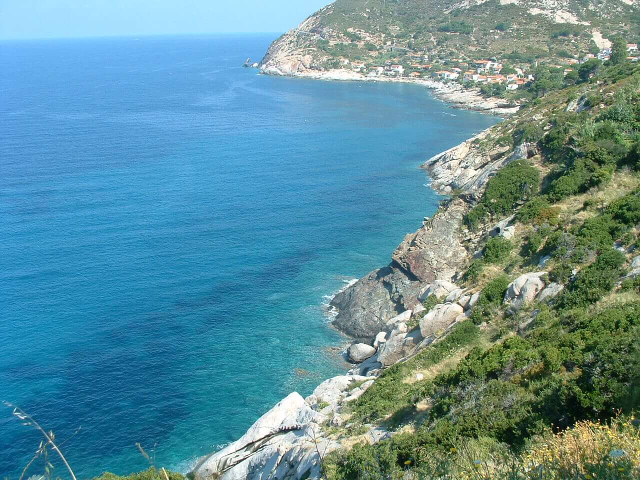 Vista panoramica della costa di Piombino, con mare blu intenso, rocce e vegetazione.