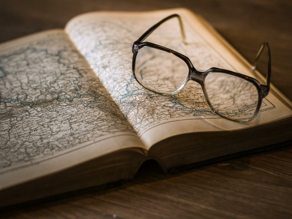 Libro aperto con una mappa dettagliata e un paio di occhiali appoggiati sopra, su un tavolo in legno, in un'atmosfera vintage.