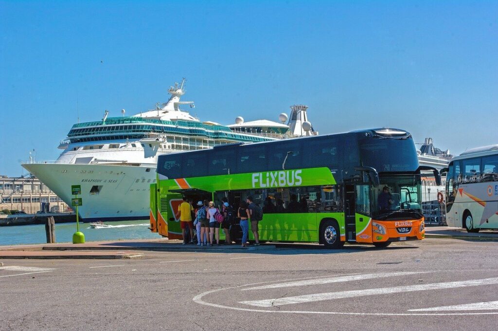 Autobus Flixbus parcheggiato vicino a una grande nave da crociera in un porto.