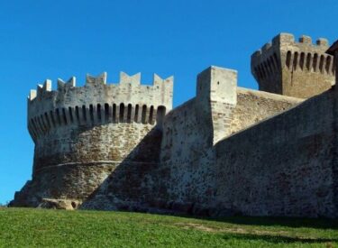 Mura e torrette del castello di Piombino sotto un cielo blu senza nuvole.