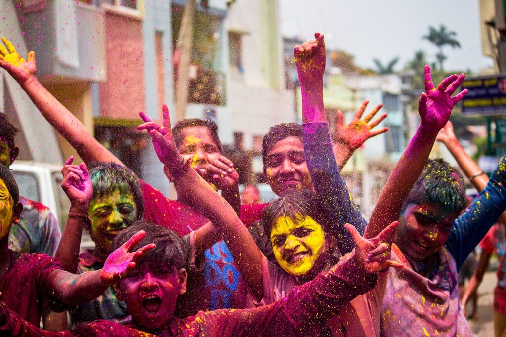 Bambini sorridenti coperti di polveri colorate durante una festa tradizionale, con mani alzate in segno di gioia.