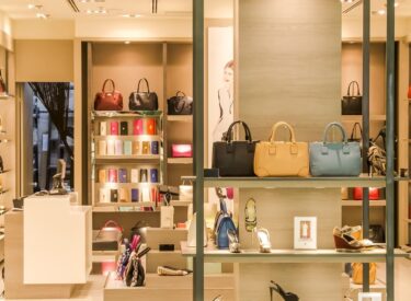 Interno di una boutique di lusso con borse eleganti, scarpe e accessori esposti su scaffali illuminati in un ambiente raffinato.