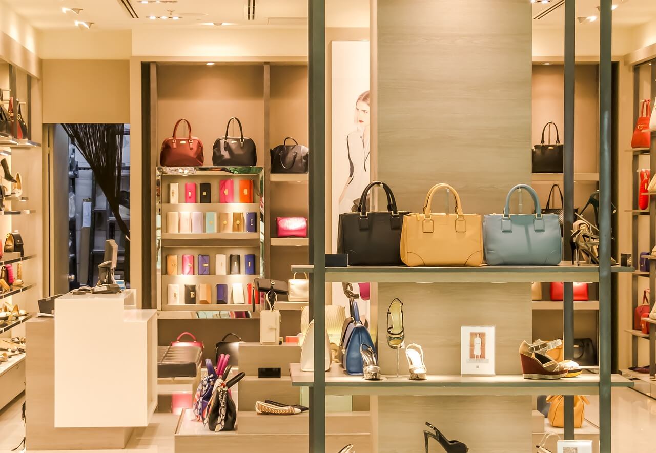 Interno di una boutique di lusso con borse eleganti, scarpe e accessori esposti su scaffali illuminati in un ambiente raffinato.