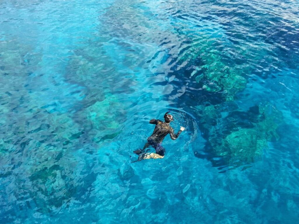 Uomo che nuota in un mare cristallino, con la superficie increspata e riflessi di luce.