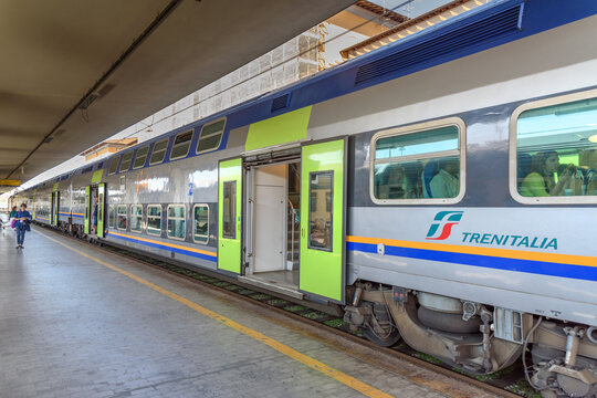 Treno regionale Trenitalia in una stazione italiana, con porte aperte e passeggeri visibili all'interno.