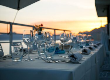 Tavola apparecchiata con bicchieri e posate su una terrazza vista mare al tramonto, creando un’atmosfera romantica ed elegante dove mangiare a Piombino