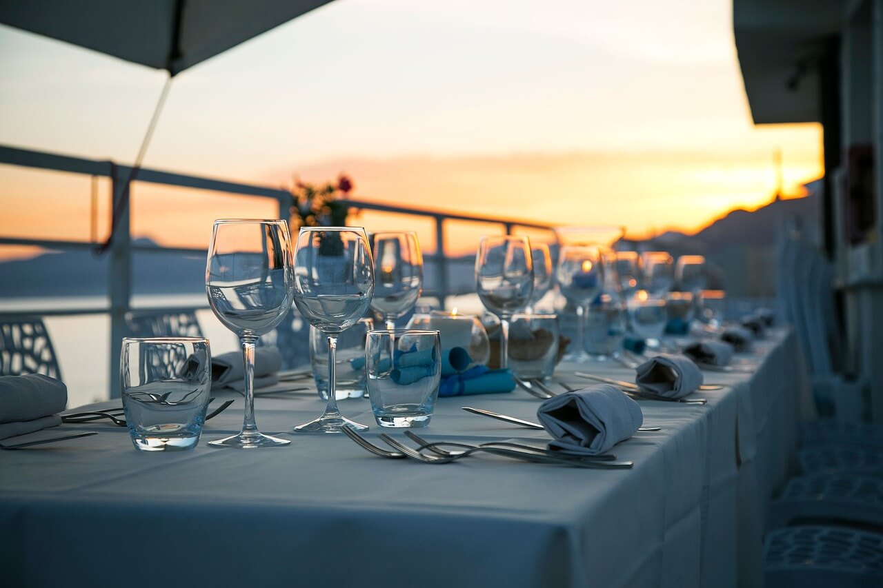 Tavola apparecchiata con bicchieri e posate su una terrazza vista mare al tramonto, creando un’atmosfera romantica ed elegante dove mangiare a Piombino