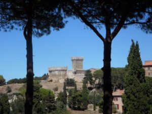 Vista del castello di Populonia medievale attraverso alberi in Toscana. Cielo sereno, architettura storica, natura rigogliosa.