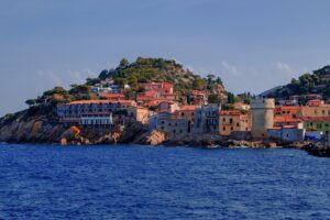 Villaggio su costa rocciosa dell’Isola del Giglio con case colorate, mare blu e scogli sul lungomare.